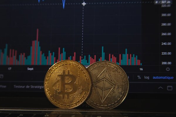 Bitcoin and Ethereum coins in front of a financial chart screen