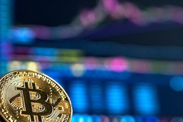 Bitcoin coin in front of cryptocurrency trading chart screen