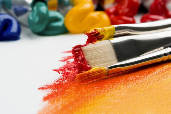 Paintbrushes with vivid red and orange paint on white canvas